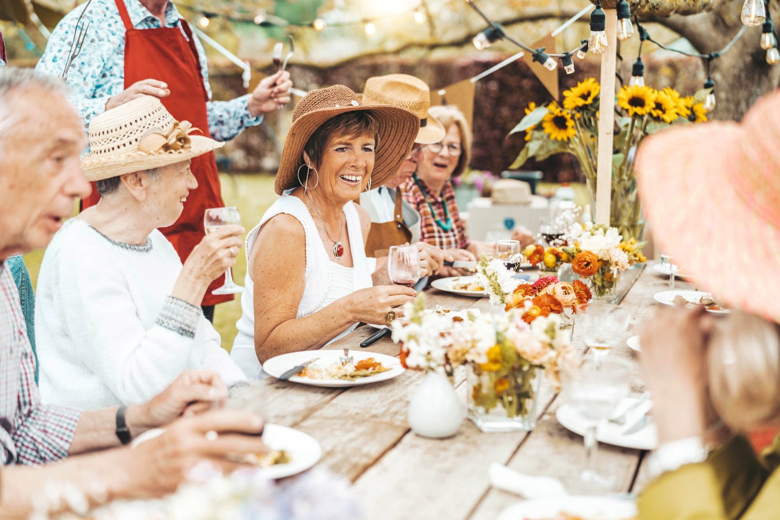 group of senior people having bbq dinner party in home garden happy family eating food and drinking wine together sitting at restaurant table